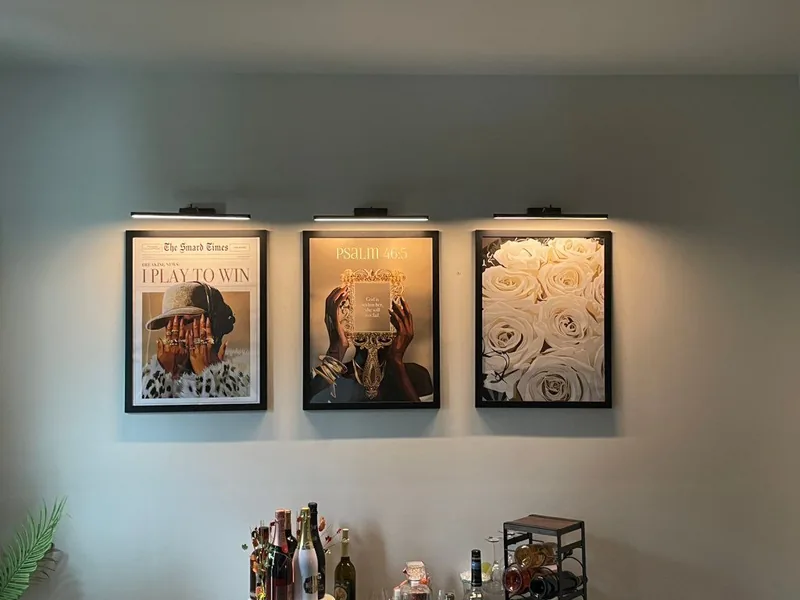 Three framed pieces mounted evenly beneath individual picture lights