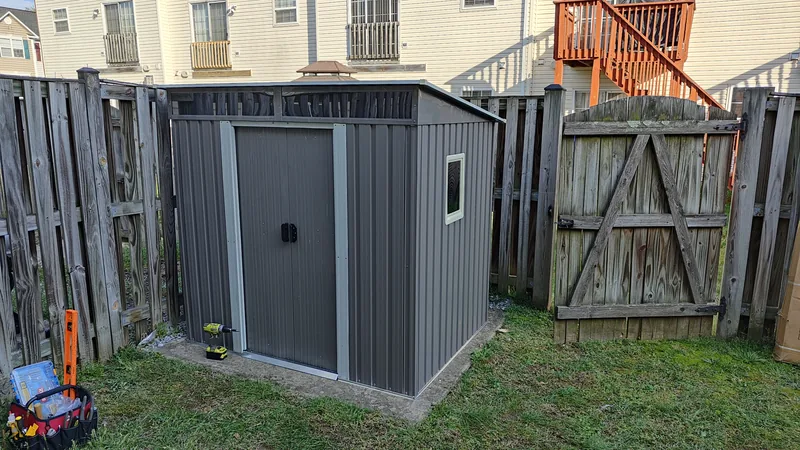 Completed gray outdoor storage shed assembled beside a fence